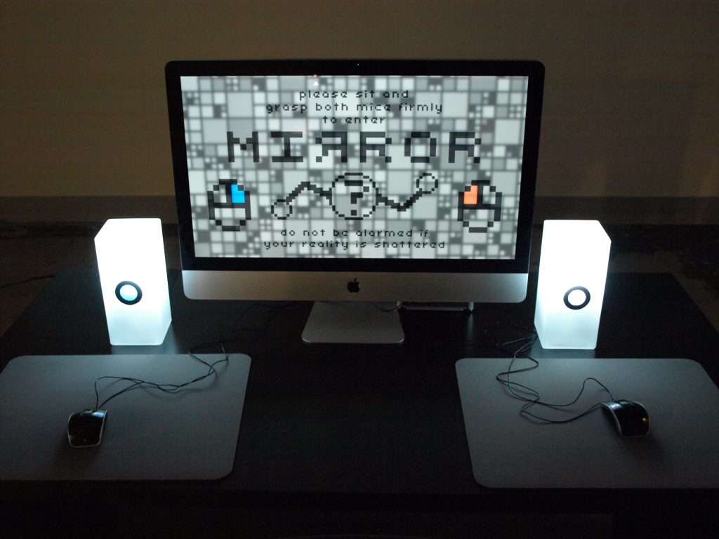 Photo of a monitor on a desk flanked by two lamps with color indicators: blue on left, red on right. There are also two computer mice, one on each side. The screen has similar colored indicators on each side as computer mouse icons.