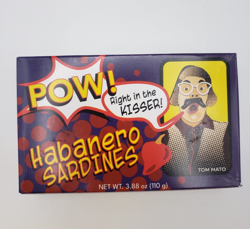 Photo of a small cardboard box with a printed design in a comic book style. The fonts look hand-drawn and the Tom Mato character, dressed as if ice fishing, is done in a halftone style. The text reads: "Pow! Right in the kisser! Habanero Sardines"